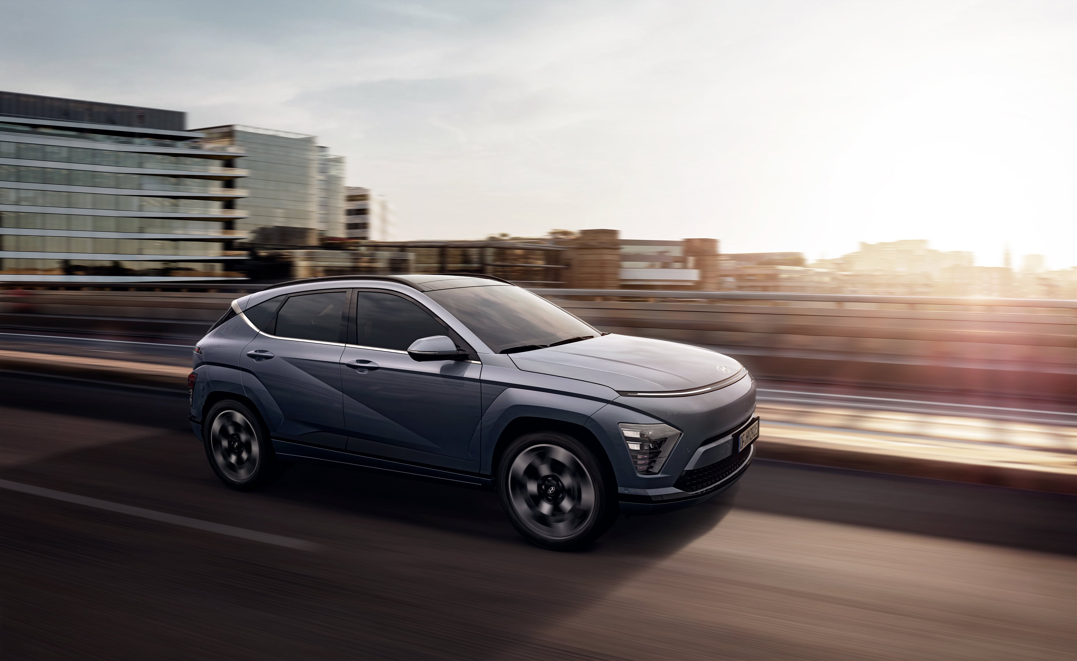 The all-new Hyundai KONA in blue is pictured driving down a city.