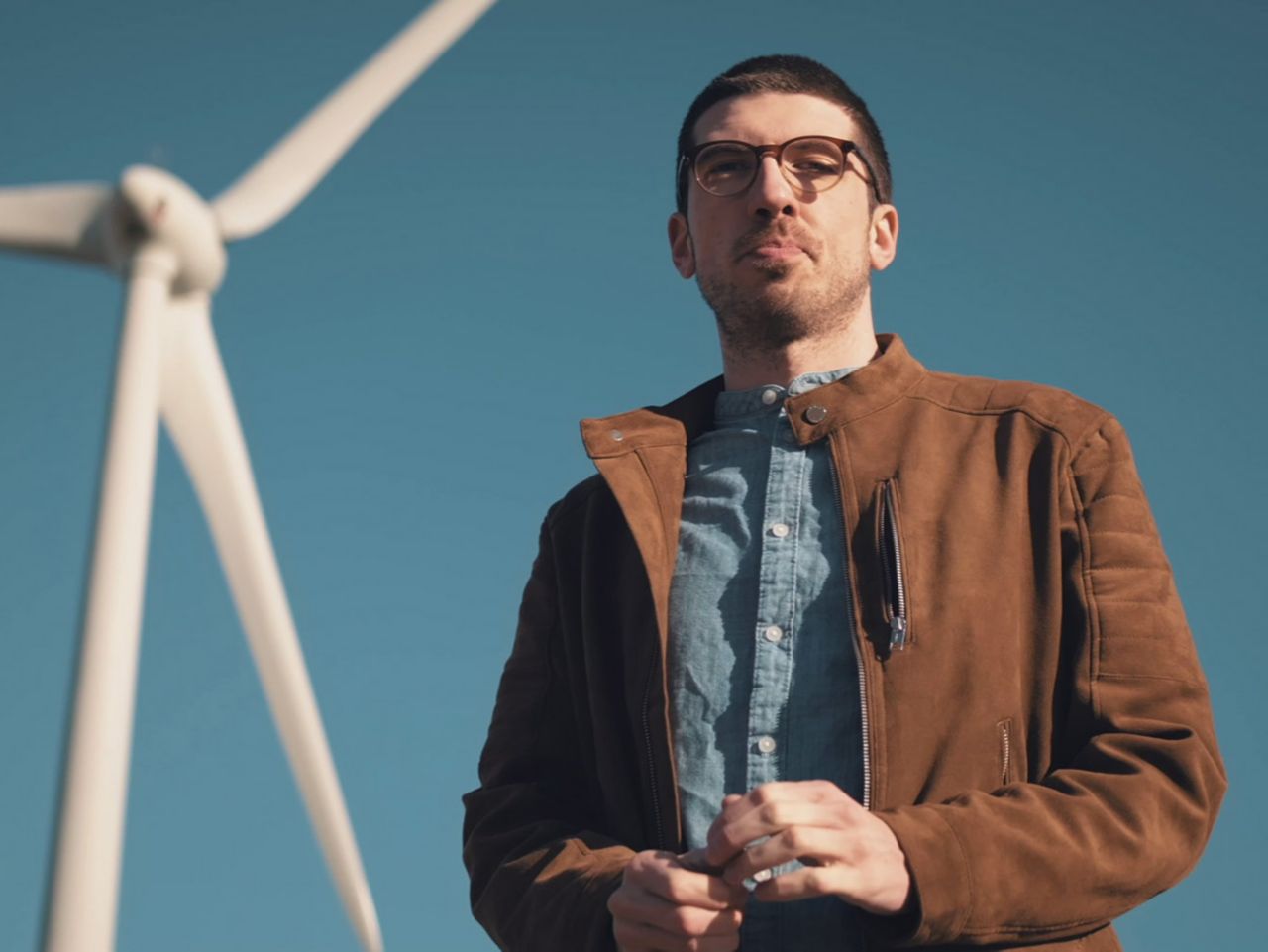 A man standing in front of a wind turbine which produces renewable energy used at IONITY stations.