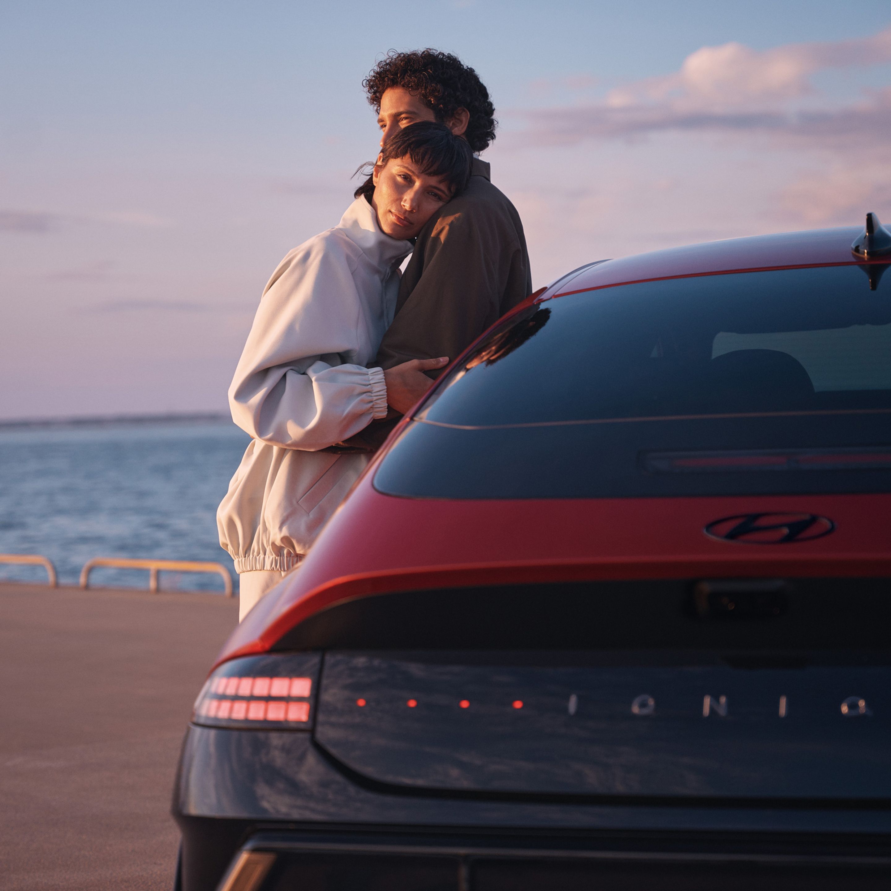 A man and a woman hugging while leaning on a Hyundai IONIQ 6 N Line parked next to the ocean.