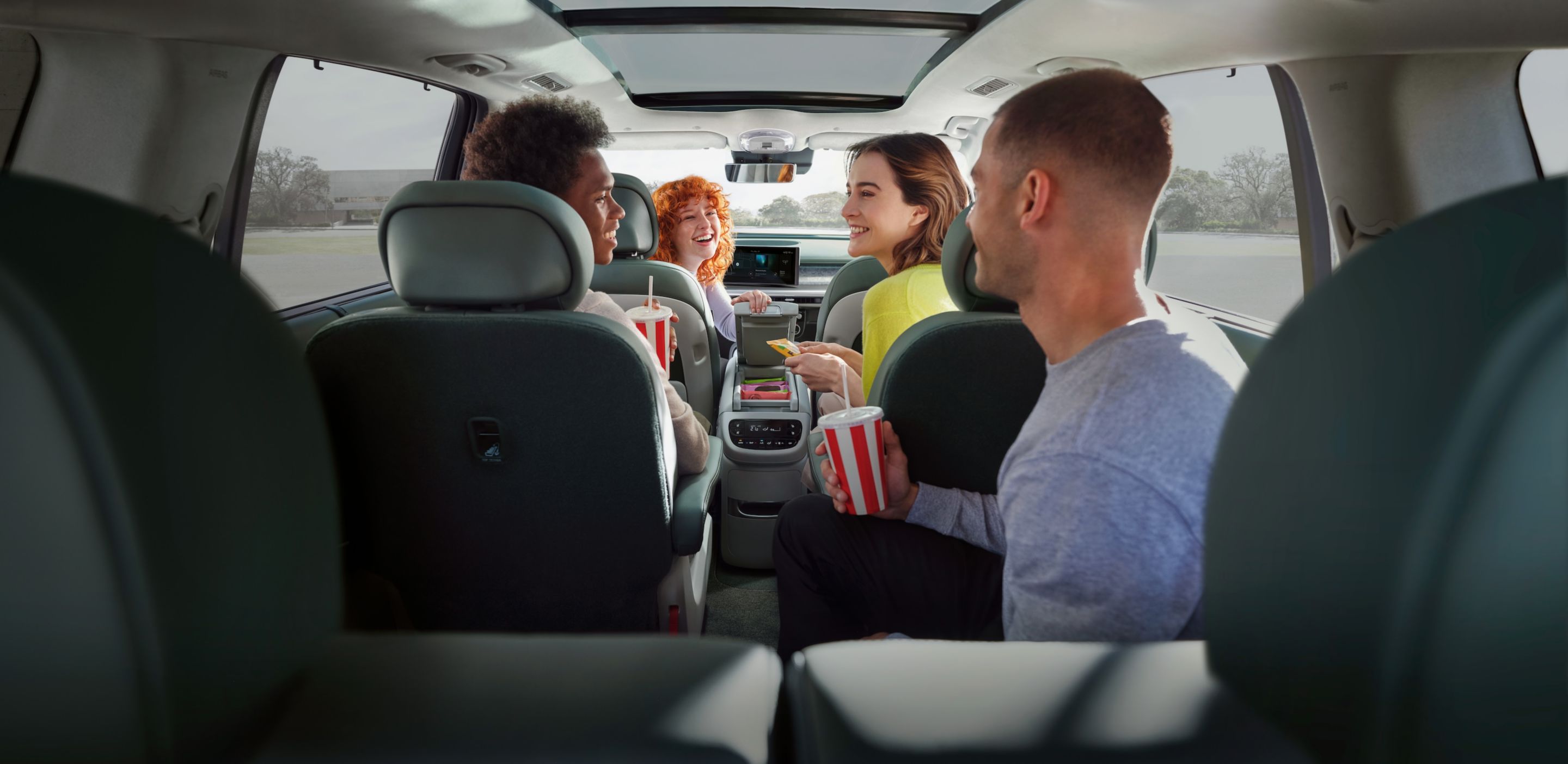 Four people in the Hyundai IONIQ 9 interior sharing snacks and drinks.