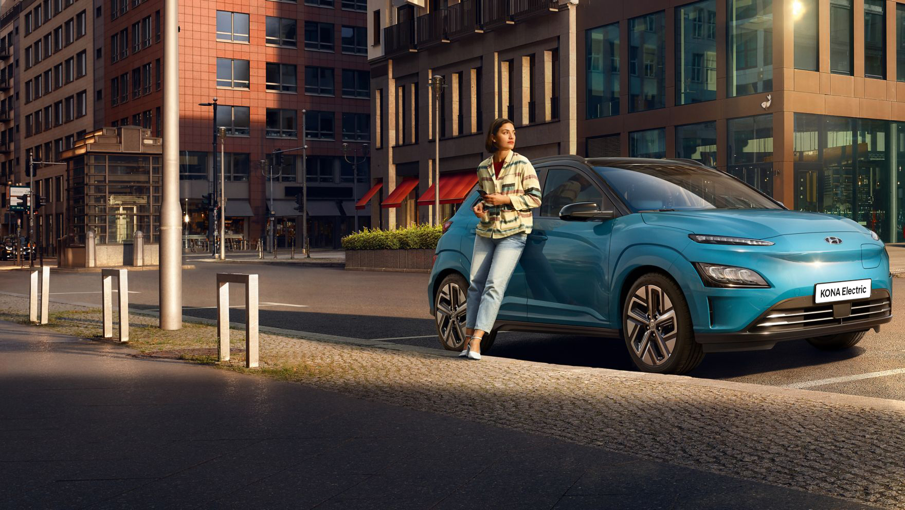 A woman leaning relaxed against the new Hyundai Kona Electric in a city.