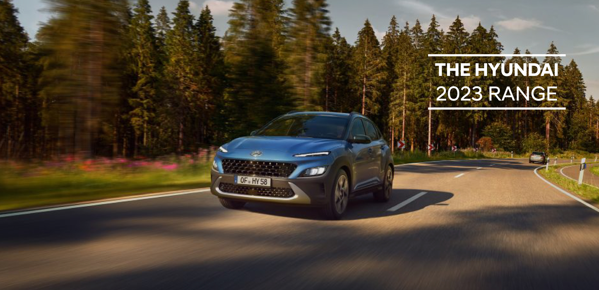 The new Hyundai Kona from the front in Surfy Blue driving down a forest road.