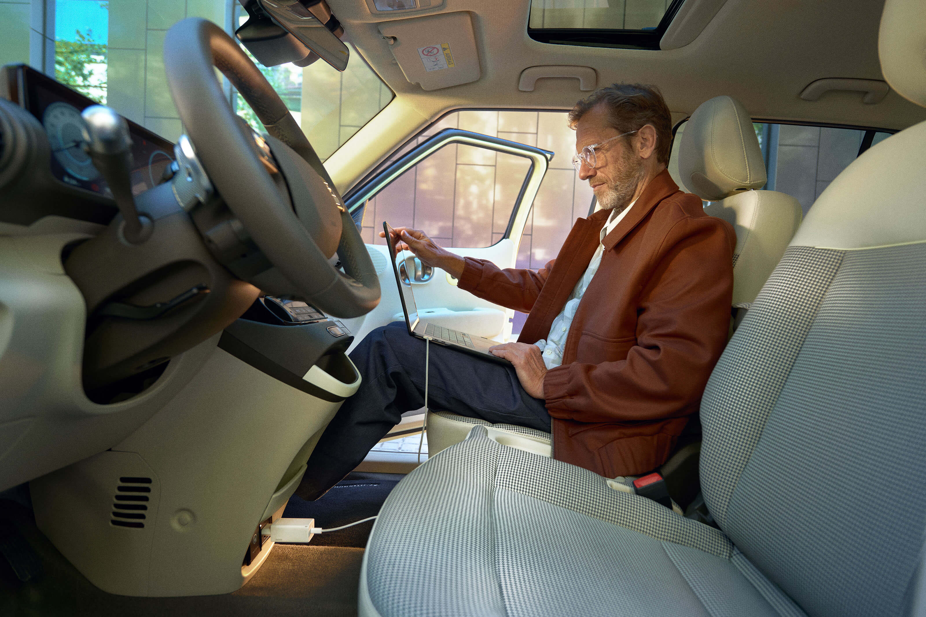 Person seated inside using a laptop powered via the vehicle's interior V2L outlet with a cable connected.