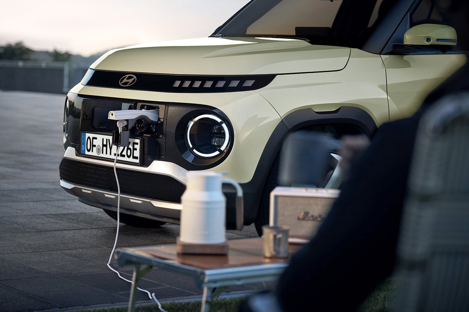 A woman poses on the new Hyundai INSTER small electric car, used as a charging station for camera equipment nearby.