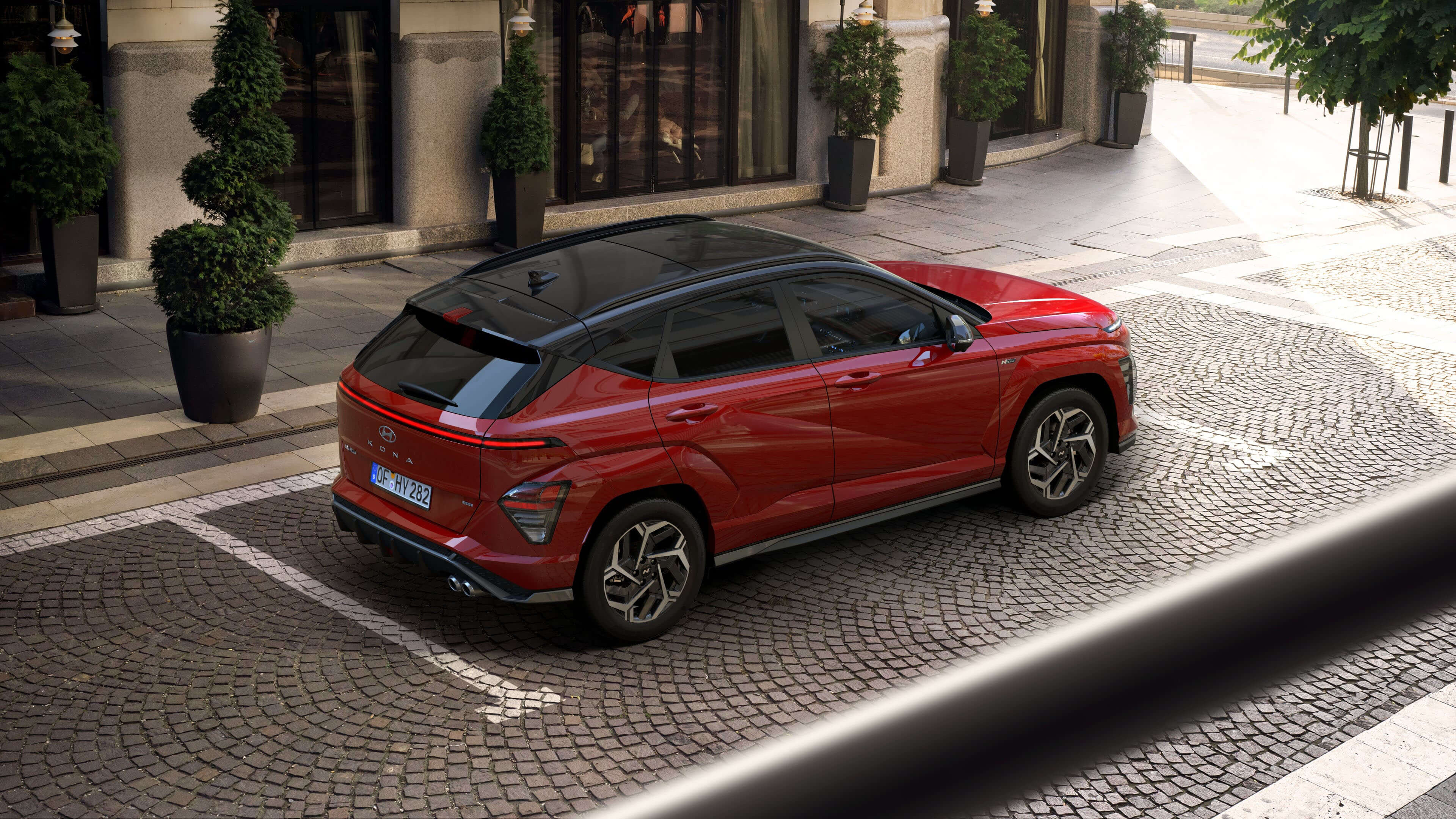 The all-new Hyundai KONA N Line in red parked in front of a building with several small trees.&nbsp;