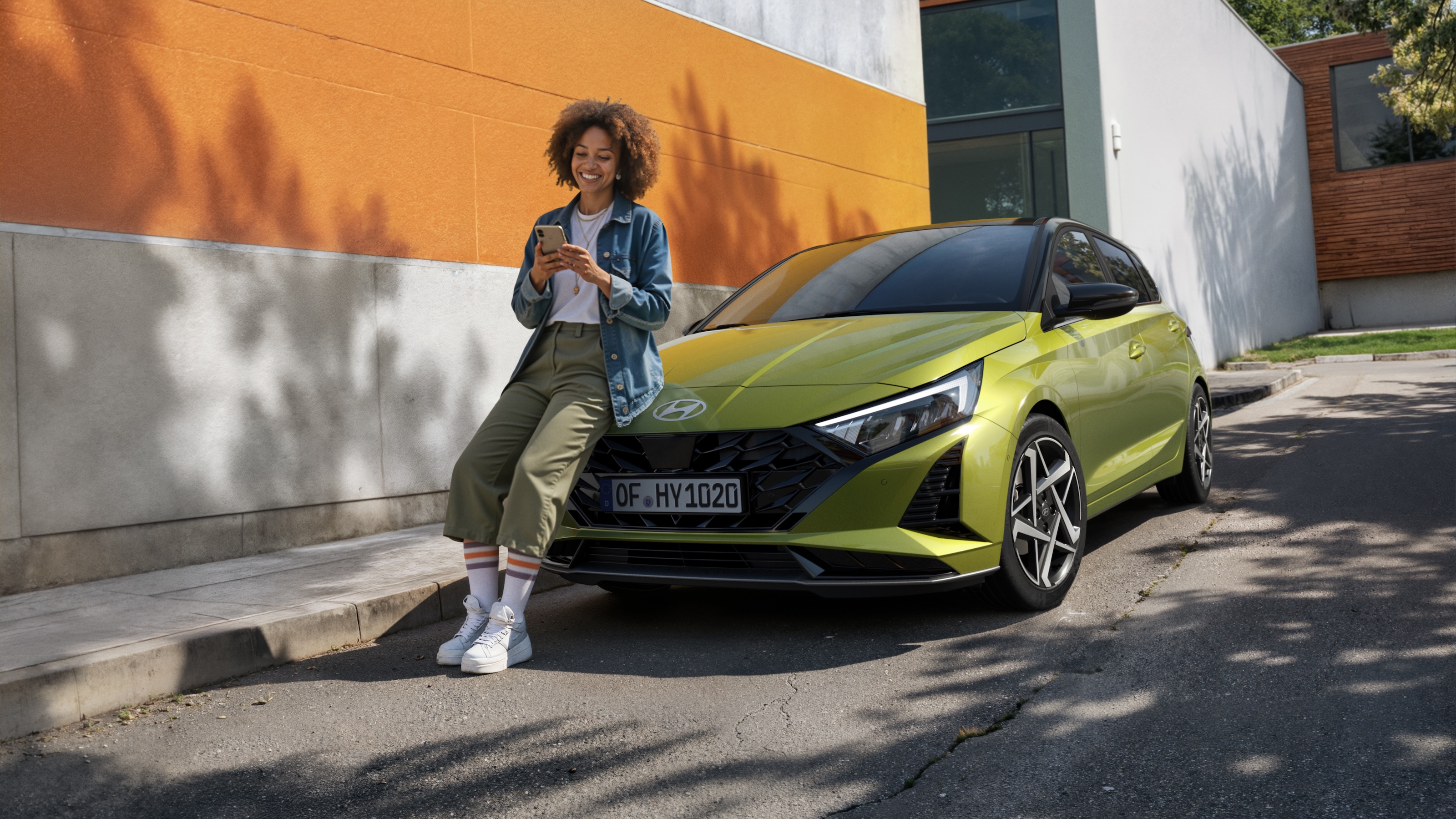 Person leaning on a Hyundai i20 while using a phone in an urban setting.