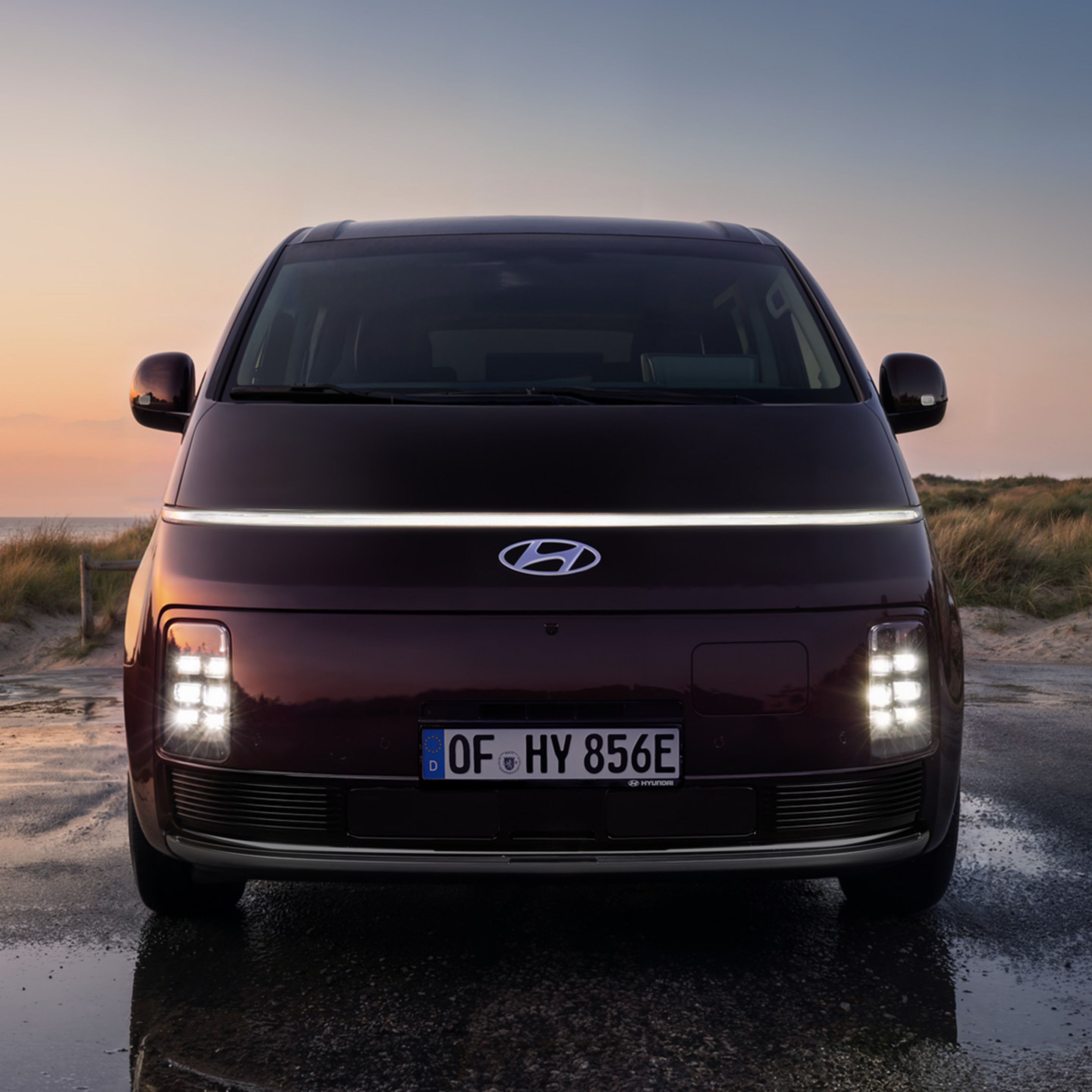 Front view of the Hyundai STARIA Electric with illuminated LED lights&nbsp;at sunset.