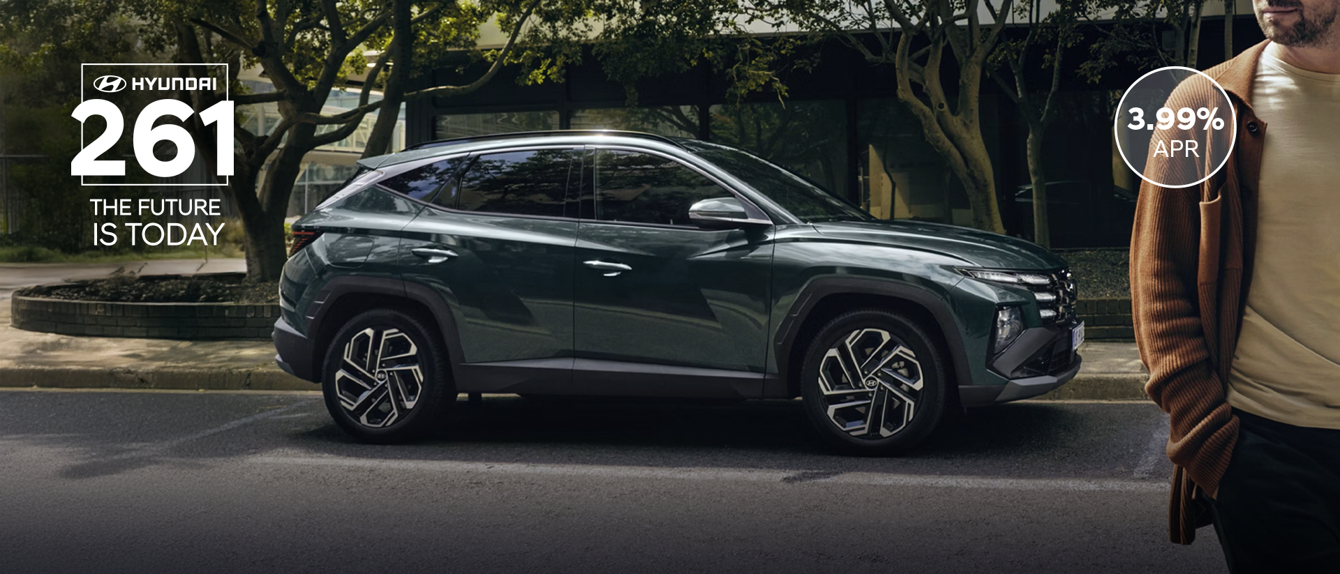A man walking near a Hyundai&nbsp;TUCSON Hybrid parked by some trees.