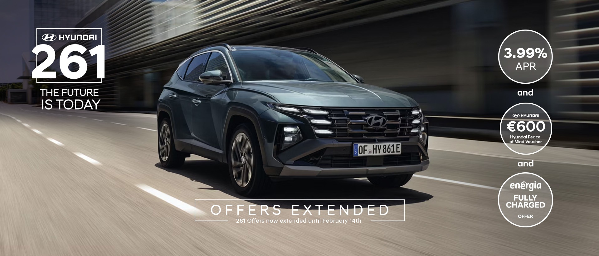 The Hyundai TUCSON Plug-in Hybrid driving down a city street with modern buildings visible.