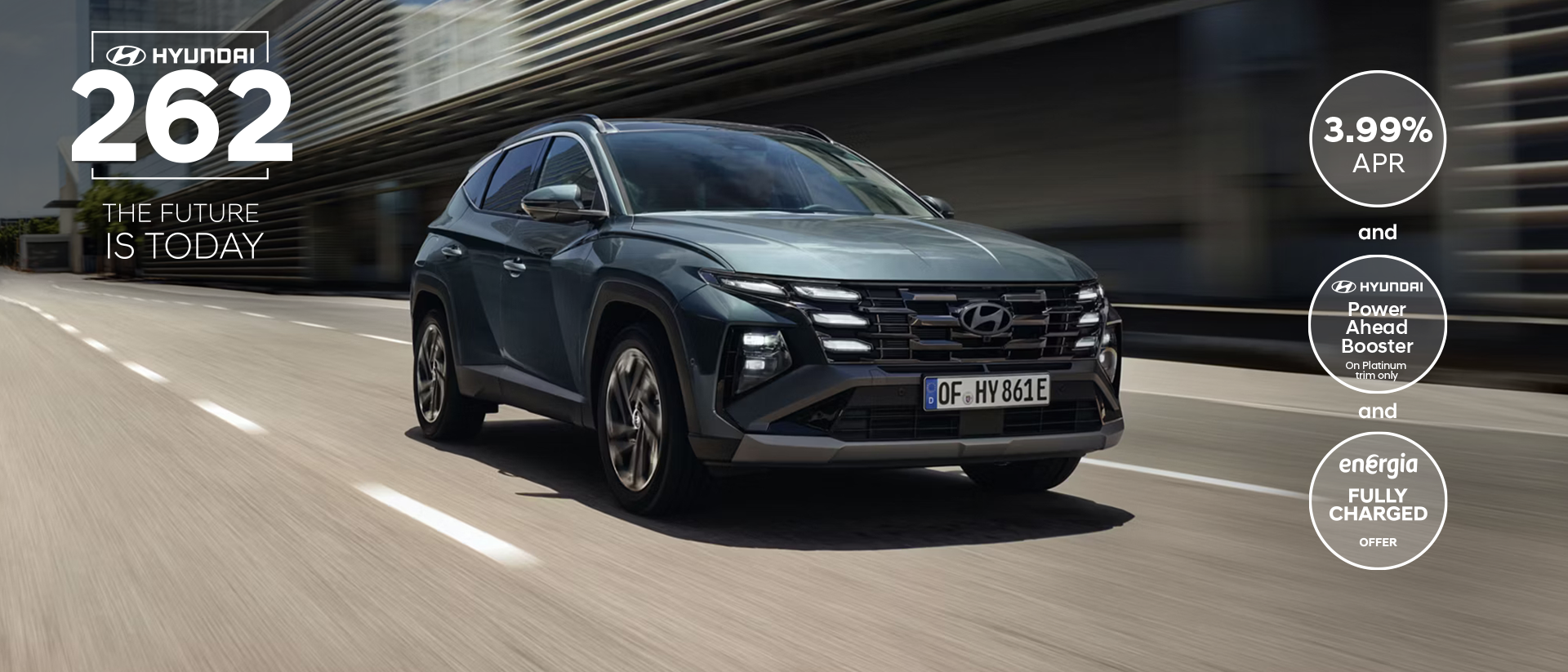 The Hyundai TUCSON Plug-in Hybrid driving down a city street with modern buildings visible.