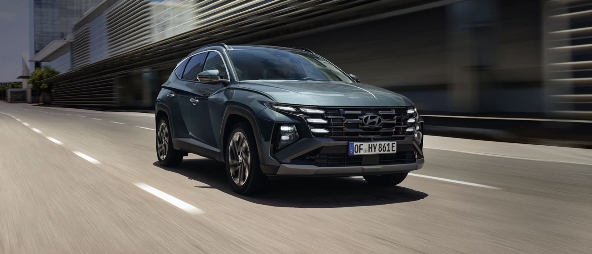 The Hyundai TUCSON Plug-in Hybrid driving down a city street with modern buildings visible.