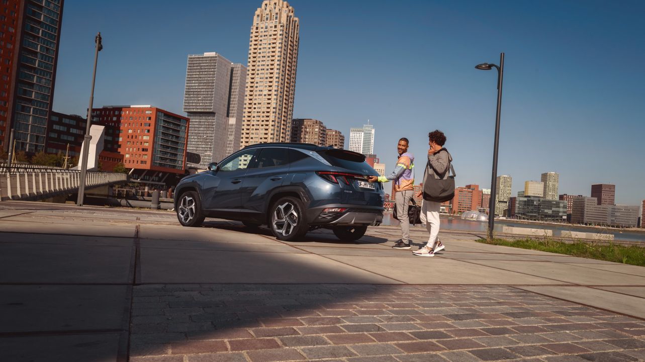 The All-New Hyundai Tucson Hybrid compact SUV parked on a city street pictured from the side.